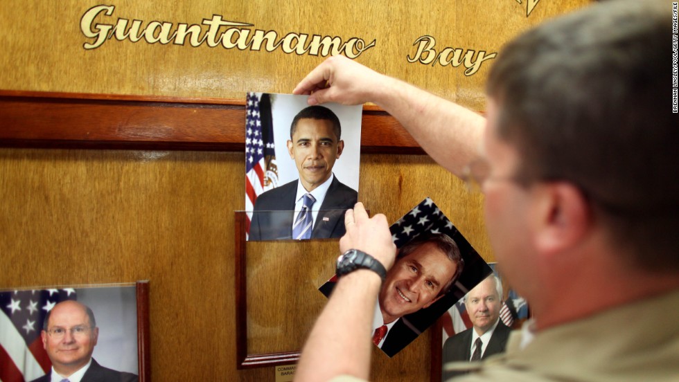 GUANTANAMO BAY, CUBA - JANUARY 20: (NOTE TO EDITORS: PHOTO HAS BEEN REVIEWED BY US MILITARY OFFICIALS) U.S. Navy Chief Petty Officer Bill Mesta replaces an official picture of outgoing President George W. Bush with that of newly- sworn-in U.S. President Barack Obama, in the lobby of the headquarters of the U.S. Naval Base January 20, 2009 in Guantanamo Bay, Cuba. Bush's eight-year presidency, which has overseen the detention of prisoners at Guantanamo and elsewhere, concluded midday today, and President Barack Obama has said he intends to close the offshore prison and move the trials to U.S. courts. (Photo by Brennan Linsley-Pool/Getty Images) *** Local Caption *** Bill Mesta