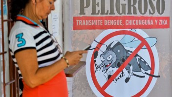 A woman checks her mobile phone next to a poster with information about the Aedes aegypti mosquito, vector of the Zika virus, on February 10, 2016, in Cali, Colombia. The World Health Organization (WHO) on Tuesday urged caution about linking the Zika virus with a rare nerve disorder called Guillain-Barre which health officials in Colombia have blamed for three deaths. AFP PHOTO / LUIS ROBAYO / AFP / LUIS ROBAYO (Photo credit should read LUIS ROBAYO/AFP/Getty Images)
