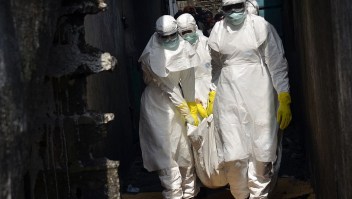 Red cross workers, wearing protective suits, carry the body of a person who died from Ebola during a burial with relatives of the victims of the virus, in Monrovia, on January 5, 2015. Schools in Ebola-ravaged Liberia will reopen in February, six months after they were closed in a bid to contain the spread of the killer virus, the education ministry said on January 5, 2015. The worst Ebola outbreak on record has killed 8,153 people over the past year. Liberia has seen the highest fatality rate with 3,471 deaths, followed by Sierra Leone and Guinea. AFP PHOTO / ZOOM DOSSO (Photo credit should read ZOOM DOSSO/AFP/Getty Images)