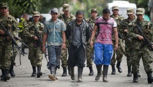 Three demobilized fighters of the 36th Column of the FARC leftist guerrillas are escorted by Colombian soldiers during a press conference on September 20, 2012 in Medellin, Antioquia department, Colombia. Seven FARC members were demobilized after surrendering their weapons. AFP PHOTO/Raul ARBOLEDA (Photo credit should read RAUL ARBOLEDA/AFP/GettyImages)