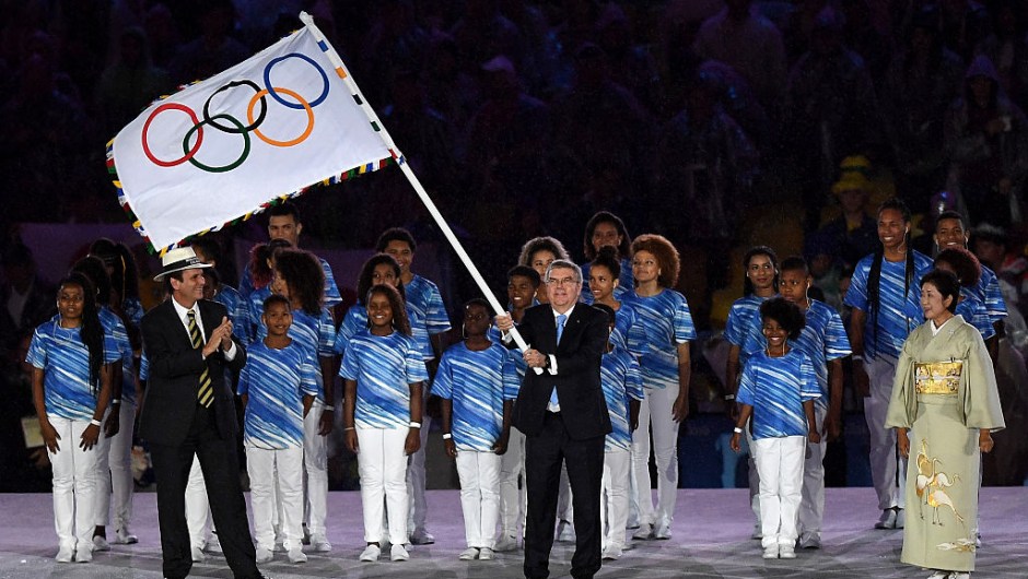 RIO DE JANEIRO, BRAZIL - AUGUST 21: IOC President Thomas Bach (C) waves the IOC flag before passing to Governor of Tokyo Yuriko Koike (R) after receiving it from the Mayor of Rio de Janeiro Eduardo Paes (L), on stage at the Flag Handover Ceremony during the Closing Ceremony on Day 16 of the Rio 2016 Olympic Games at Maracana Stadium on August 21, 2016 in Rio de Janeiro, Brazil. (Photo by Pascal Le Segretain/Getty