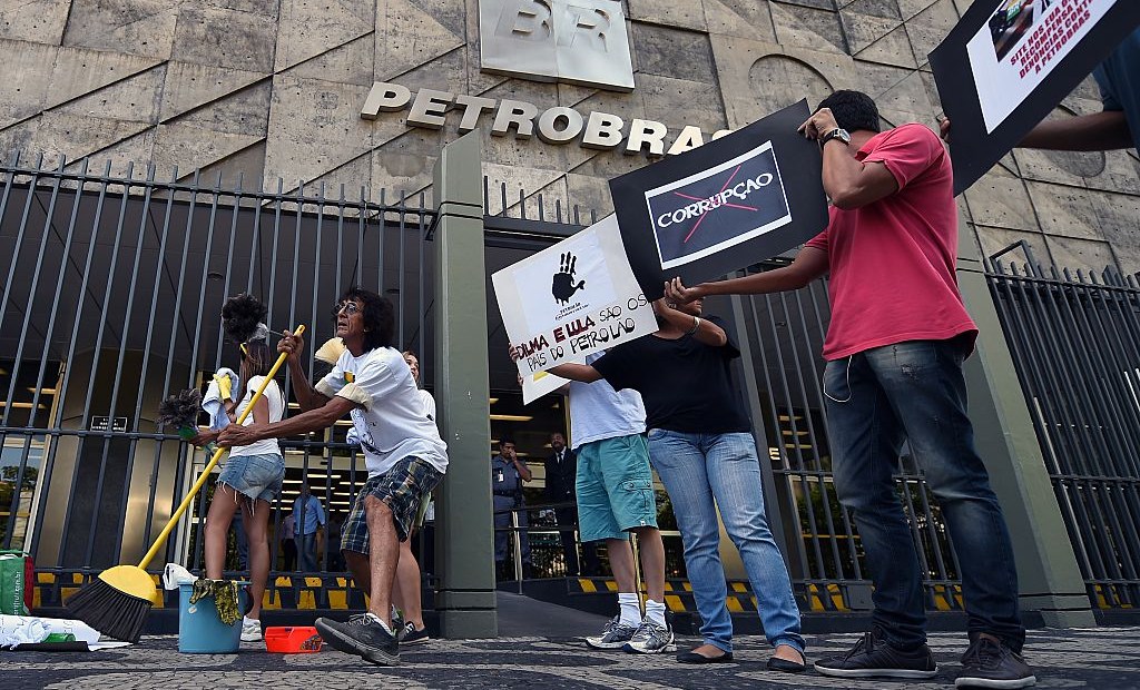 Activists hold signs during a protest against corruption outside state-owned oil giant Petrobras in Rio de Janeiro on December 16, 2014. AFP PHOTO/VANDERLEI ALMEIDA (Photo credit should read VANDERLEI ALMEIDA/AFP/Getty Images)