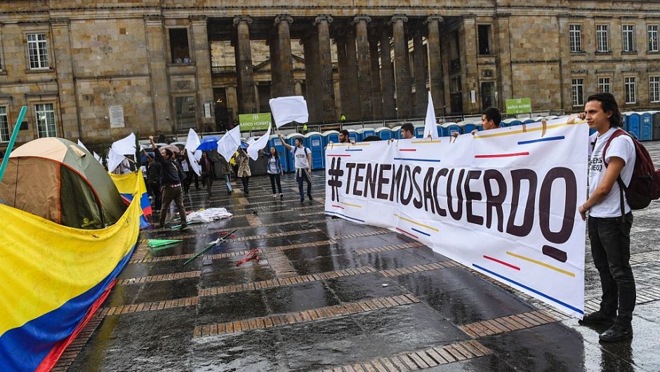 People hold a sign reading "We have an agreement" and flutter white flags during a demo for the immediate implementation of the agreement between the Colombian government and the FARC guerrillas at Bolivar Square in Bogota on November 18, 2016. / AFP / Luis Acosta (Photo credit should read LUIS ACOSTA/AFP/Getty Images)