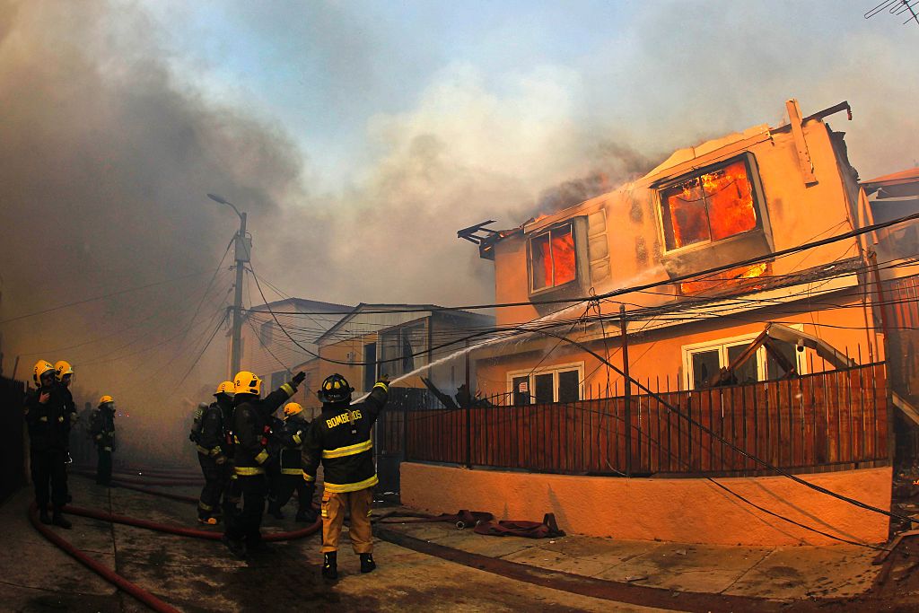 Firefighters work to extinguish the flames from a house in Valparaiso, Chile, on January 02, 2017 as the fire threatens to reach the city's port, authorities have declared a red alert in the area. / AFP / ATON CHILE / Sebastián CISTERNAS / (Photo credit should read SEBASTIAN CISTERNAS/AFP/Getty Images)