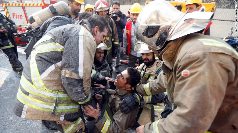 Bomberos iraníes consuelan a un compañero, tras el colapso del edificio.