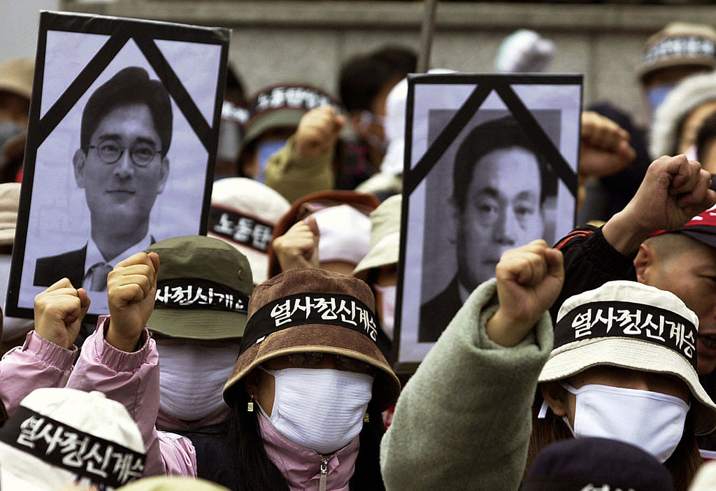 EOUL, REPUBLIC OF KOREA: South Korean workers chant slogan and hold black ribbon pictures of Lee Kun Hee (R) Chairman of the Samsung Group and his son Lee Jae-Yong (L) during a protest rally in Seoul, 12 November 2003. Tens of thousands of workers launched a one-day nationwide strike Wednesday as militant labor union leaders violated a police ban to stage a protest rally against government policy. The Korean Confederation of Trade Unions (KCTU) said some 150,000 workers joined the stoppage at 120 workplaces, including South Korea's largest auto company, Hyundai Motor, in the southern city of Ulsan.The labor ministry said the walkout had no major impact on the economy, saying it 44,000 workers from 77 metal, textile and chemical firms across the country.AFP PHOTO/JUNG YEON-JE (Photo credit should read JUNG YEON-JE/AFP/Getty Images)