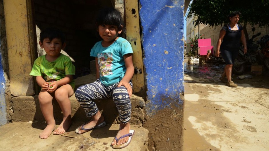 Children sit on their doorstep in the town of Huarmey, 300 kilometres north of Lima, where the ground was covered on March 19, 2017 with several centimetres of mud and silt after a flash flood hit the evening before. The El Nino climate phenomenon is causing muddy rivers to overflow along the entire Peruvian coast, isolating communities and neighbourhoods. Thousands have been affected since January, and 72 people have died. Most cities face water shortages as water lines have been compromised by mud and debris. / AFP PHOTO / CRIS BOURONCLE (Photo credit should read CRIS BOURONCLE/AFP/Getty Images)