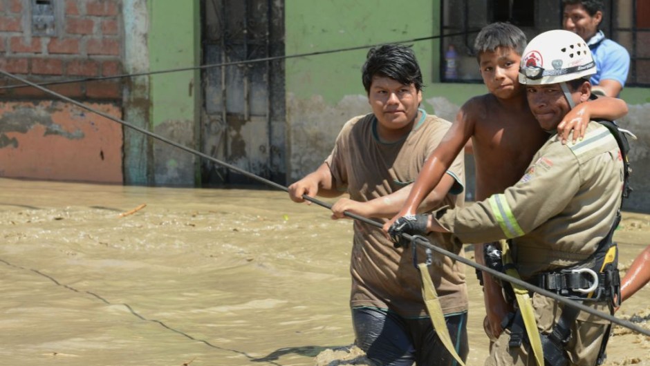 Rescue workers help local residents of the town of Huarmey, 300 kilometres north of Lima, wade through muddy water in the street on March 19, 2017 after a flash flood hit the evening before. The El Nino climate phenomenon is causing muddy rivers to overflow along the entire Peruvian coast, isolating communities and neighbourhoods. Thousands have been affected since January, and 72 people have died. Most cities face water shortages as water lines have been compromised by mud and debris. / AFP PHOTO / CRIS BOURONCLE (Photo credit should read CRIS BOURONCLE/AFP/Getty Images)