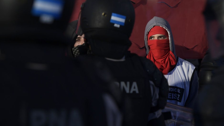 TOPSHOT - A masked protester stands next to members of Prefectura Naval Argentina who guard the entrance of Pueyrredon bridge blocked by demonstrators in Avellaneda, Buenos Aires on April 6, 2017, during a 24 hours general strike. A 24 hours general strike was called by worker's unions demanding to President Mauricio Macri's government to take measures against inflation and keep campaign promises. / AFP PHOTO / JUAN MABROMATA (Photo credit should read JUAN MABROMATA/AFP/Getty Images)