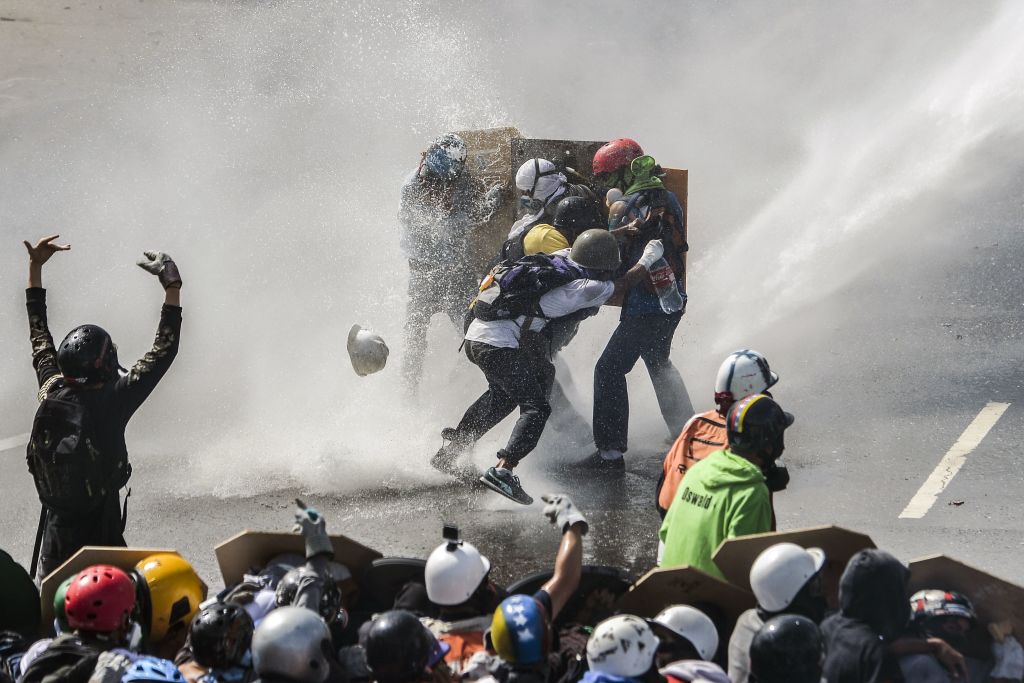 TOPSHOT - Opposition activists are hit by the jet of a riot police water cannon during a protest against President Nicolas Maduro in Caracas, on May 10, 2017. Both the Venezuelan government and the opposition admit that violent protests that have gripped the country for nearly two months are out of control -- and analysts warn they could be a double-edged sword that might trigger even more unrest. / AFP PHOTO / LUIS ROBAYO (Photo credit should read LUIS ROBAYO/AFP/Getty Images)