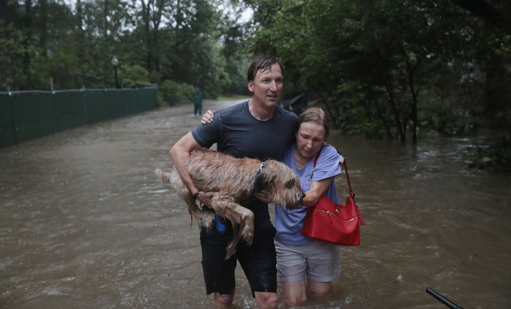 HOUSTON, TX - AUGUST 27: Andrew White (L) helps a neighbor down a street after rescuing her from her home in his boat in the upscale River Oaks neighborhood after it was inundated with flooding from Hurricane Harvey on August 27, 2017 in Houston, Texas. Harvey, which made landfall north of Corpus Christi late Friday evening, is expected to dump upwards to 40 inches of rain in Texas over the next couple of days. (Photo by Scott Olson/Getty Images)