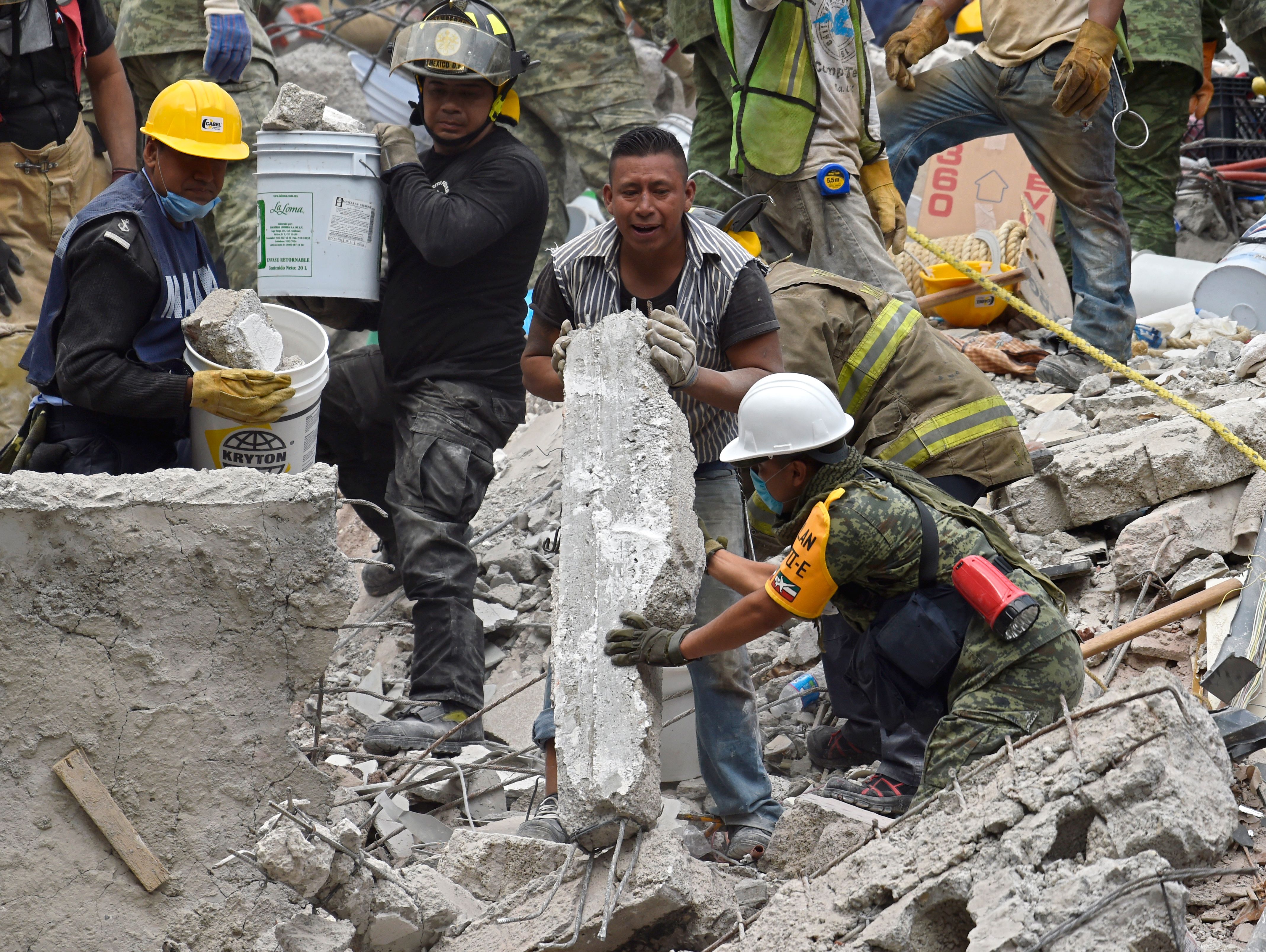 A marine, a firefighter, a volunteer and a soldier work together in the removal of debris of a flattened building in Mexico City on September 20, 2017 as the search for survivors continues a day after a strong quake hit central Mexico. A powerful 7.1 earthquake shook Mexico City on Tuesday, causing panic among the megalopolis' 20 million inhabitants on the 32nd anniversary of a devastating 1985 quake. / AFP PHOTO / Pedro PARDO (Photo credit should read PEDRO PARDO/AFP/Getty Images)