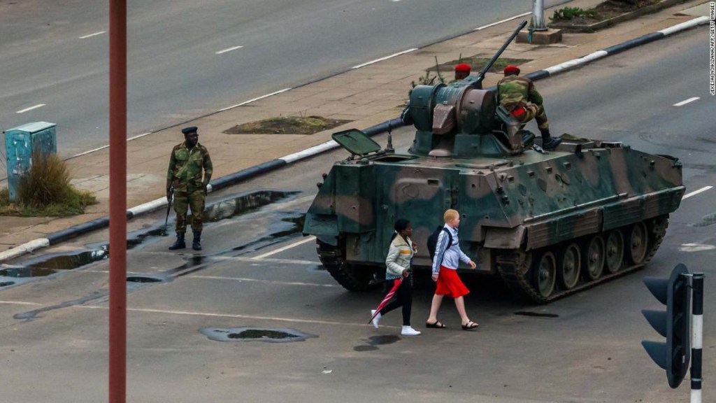 Young women walk past an armoured personnel carrier that stations by an intersection as Zimbabwean soldiers regulate traffic in Harare on November 15, 2017. Zimbabwe's military appeared to be in control of the country on November 15 as generals denied staging a coup but used state television to vow to target "criminals" close to President Mugabe. / AFP PHOTO / Jekesai NJIKIZANA (Photo credit should read JEKESAI NJIKIZANA/AFP/Getty Images)