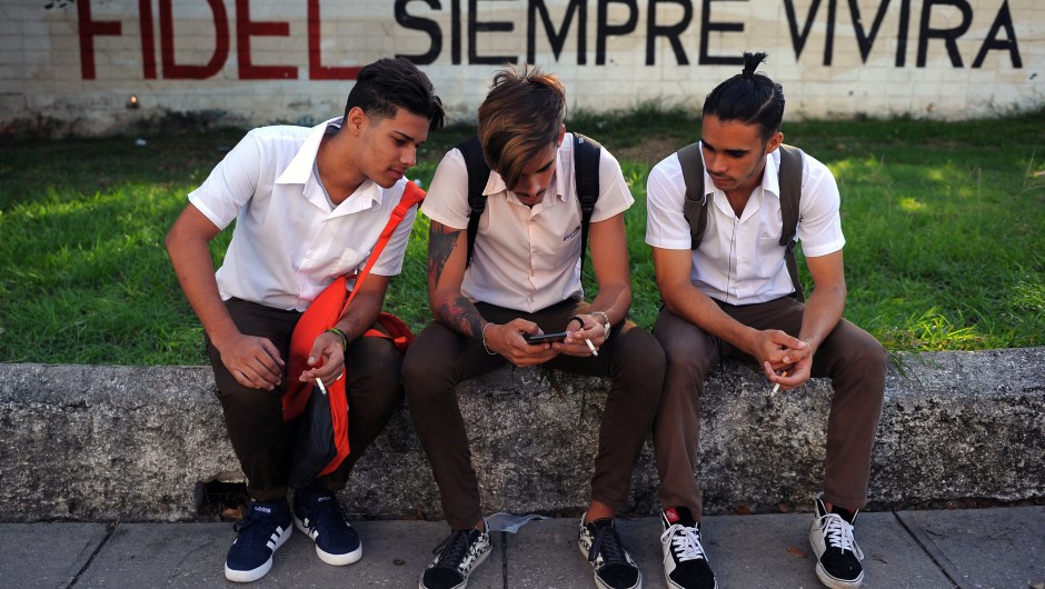 Cuban youngsters look at a cellphone as they sit in front of a graffiti reading "Fidel (Castro) will always live" in Havana on November 24, 2017. Cuba commemorates on November 25 the first anniversary of the death of Fidel Castro, focused on an electoral process that will imply a presidential change, in a framework of economic regression, hostility from the United States, and stagnation in its reforms. / AFP PHOTO / YAMIL LAGE (Photo credit should read YAMIL LAGE/AFP/Getty Images)
