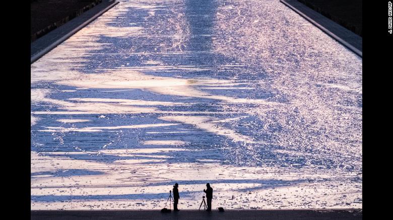 Two photographers are silhouetted against the frozen surface of the Reflecting Pool on the National Mall in Washington as they capture the first sunrise of the new year, Monday, Jan. 1, 2018. (AP Photo/J. David Ake)