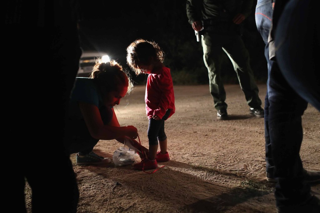 La madre de la niña quita los cordones de sus zapatos, según le pidieron los agentes fronterizos. (Crédito: John Moore/Getty Images)