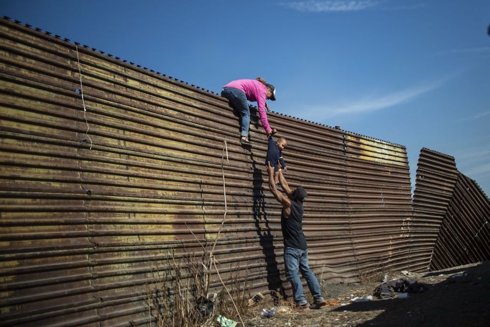 TOPSHOT - A group of Central American migrants climb the border fence between Mexico and the United States, near El Chaparral border crossing, in Tijuana, Baja California State, Mexico, on November 25, 2018. - Hundreds of migrants attempted to storm a border fence separating Mexico from the US on Sunday amid mounting fears they will be kept in Mexico while their applications for a asylum are processed. An AFP photographer said the migrants broke away from a peaceful march at a border bridge and tried to climb over a metal border barrier in the attempt to enter the United States. (Photo by Pedro PARDO / AFP) (Photo credit should read PEDRO PARDO/AFP/Getty Images)