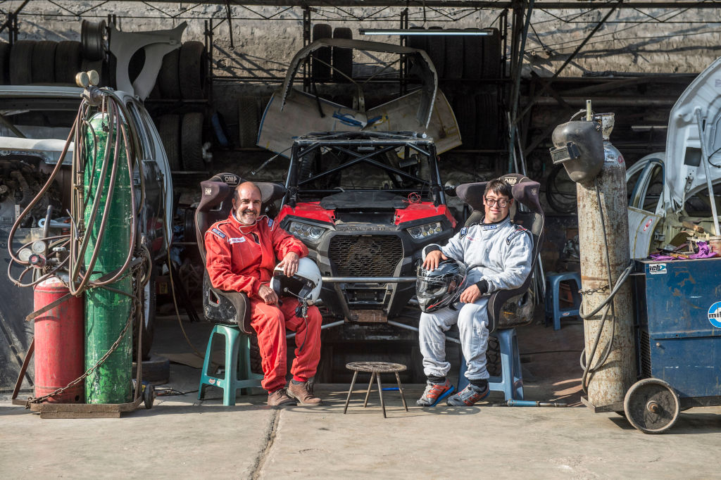 Jacques Barron (L) and his son and co-driver Lucas Barron, 25, pose at a mechanics workshop in Lima, on December 18, 2018, where their car is being prepared to take part in the upcoming Rally Dakar on January 2019. - Lucas Barron will make history on January 6 when he lines up on the Dakar 2019 start line in Peru, the first person with Down Syndrome to take part in the gruelling race. The 25-year-old, who will be co-pilot for his father Jacques, will tackle the world's most demanding rally: a 5,000 kilometer (3,000 miles), 10-day marathon, 70 percent of which will be raced over sand. (Photo by ERNESTO BENAVIDES / AFP) (Photo credit should read ERNESTO BENAVIDES/AFP/Getty Images)