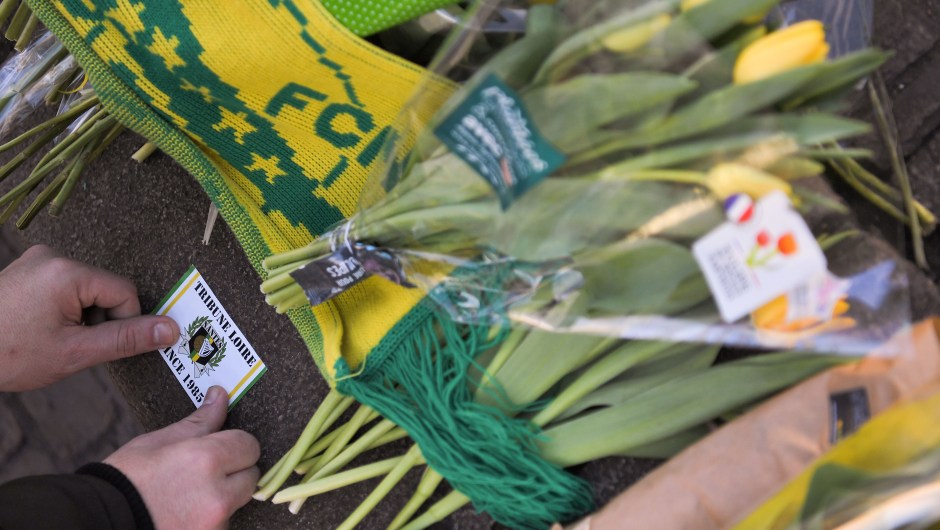 A FC Nantes football club supporter places a sticker close to flowers placed in the main square of the city of Nantes, western France, two days after it was announced that the plane carrying Argentinian forward Emiliano Sala vanished during a flight from Nantes to Cardiff in Wales, on January 23, 2019. - The 28-year-old Argentine striker is one of two people still missing after contact was lost with the light aircraft he was travelling on, on January 21, 2019 night. Sala was on his way to the Welsh capital to train with his new teammates for the first time after completing a £15 million pounds sterling ($19 million US dollars) move to Cardiff City from French side Nantes on January 19. (Photo by LOIC VENANCE / AFP) (Photo credit should read L
