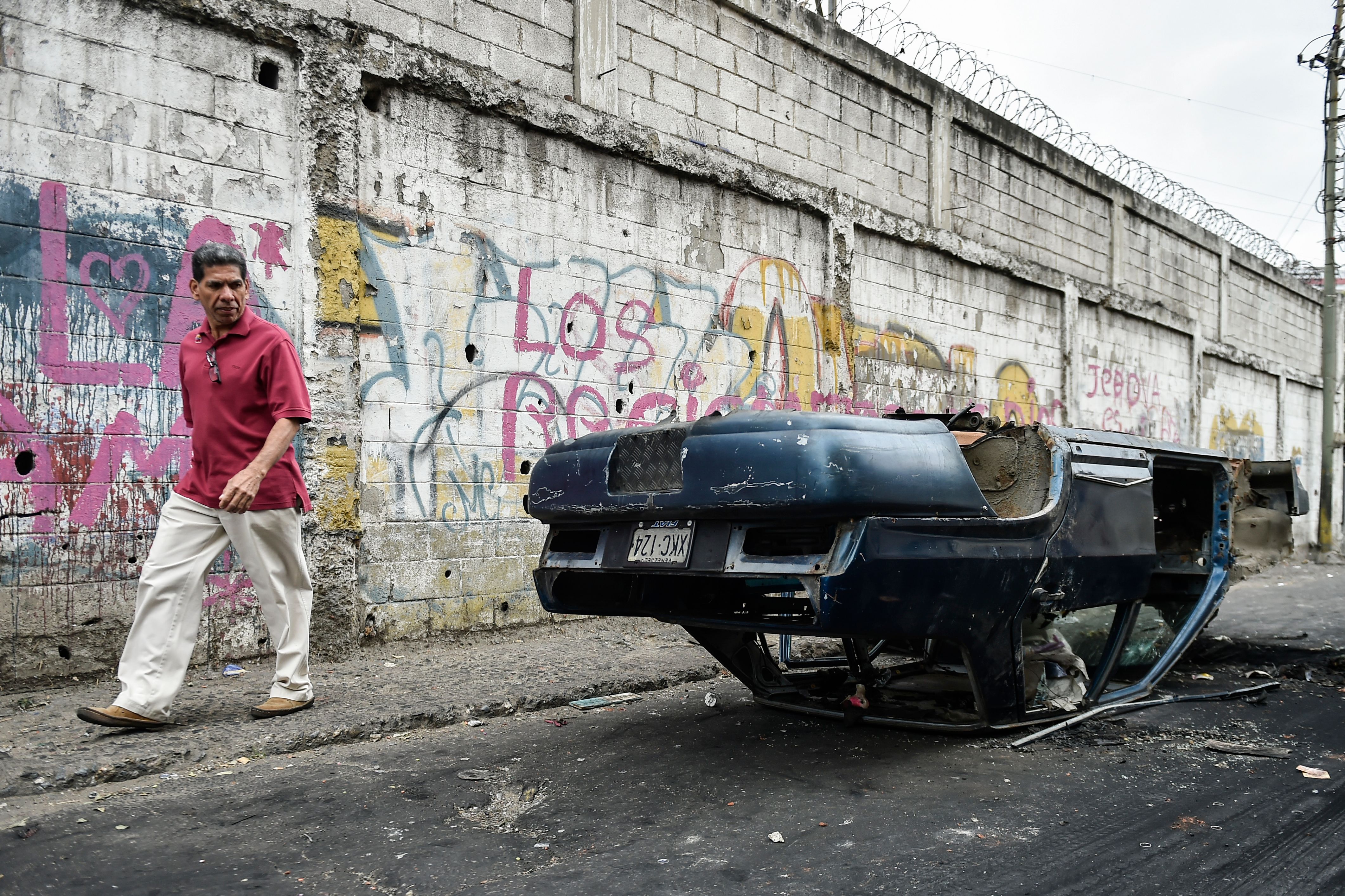 OPSHOT - A man walks by a car that was vandalised in Caracas on the eve of a march called by Venezuelan opposition on the anniversary of 1958 uprising that overthrew military dictatorship, on January 23, 2019. - At least four people have died following overnight clashes ahead of Wednesday's rival protests in Venezuela by supporters and opponents of President Nicolas Maduro, two days after a failed mutiny by soldiers hoping to spark a movement that would overthrow Maduro, police and non-governmental organizations said. (Photo by LUIS ROBAYO / AFP)        (Photo credit should read LUIS ROBAYO/AFP/Getty Images)