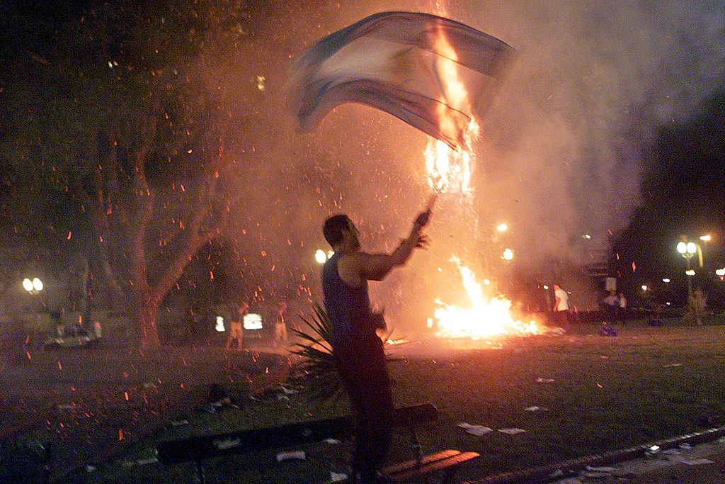 A man waves an Argentine flag at the Plaza de Mayo in Buenos Aires 20 December 2001 after Argentine police used tear gas to disperse demonstrators. Argentine Economy Minister Domingo Cavallo has resigned in the face of mounting unrest over the country's crumbling economy, local media reported early 20 December. The police action came after tens of thousands of people filled the streets of Buenos Aires to protest President Fernando de la Rua's decision to resort to emergency measure to calm unrest sparked by the crumbling Argentine economy. Five people were killed and more than 100 injured in protests and lootings of supermarkets across the country. (Photo credit should read FABIAN GREDILLAS/AFP/Getty Images)