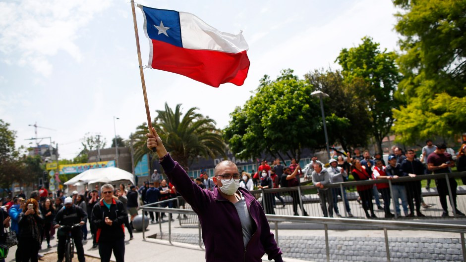 TOPSHOT - A demonstrator waves a chilean flag outside of the Plaza Maipu metro station during clashes between protesters and the riot police at Plaza de Maipu in Santiago, on October 19, 2019. - Chile's president declared a state of emergency in Santiago Friday night and gave the military responsibility for security after a day of violent protests over an increase in the price of metro tickets. (Photo by Pablo VERA / AFP) (Photo by PABLO VERA/AFP via Getty Images)