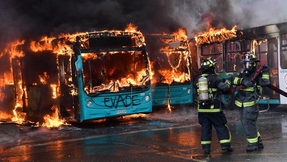 TOPSHOT - Chilean firefighters extinguish a burning bus during clashes between protesters and the riot police in Santiago, on October 19, 2019. - Chile's president declared a state of emergency in Santiago Friday night and gave the military responsibility for security after a day of violent protests over an increase in the price of metro tickets. (Photo by Martin BERNETTI / AFP) (Photo by MARTIN BERNETTI/AFP via Getty Images)