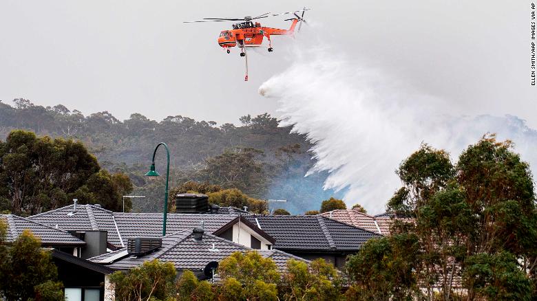 A skycrane drops water on a bushfire in scrub behind houses in Bundoora, Melbourne, Monday, Dec. 30, 2019. New Year???s Eve fireworks in Australia???s capital and other cities have been canceled as the wildfire danger worsens in oppressive summer heat, and pressure was building for Sydney???s iconic celebrations to be similarly scrapped.(Ellen Smith/AAP Images via AP)