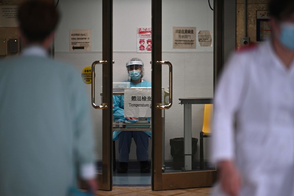 TOPSHOT - A medical worker wearing protective gear (C) waits to take the temperature of people in an entrance of Princess Margaret Hospital in Hong Kong on February 4, 2020. - Hong Kong on February 4 become the second place outside of the Chinese mainland to report the death of a patient being treated for a new coronavirus that has so far claimed more than 400 lives. (Photo by Anthony WALLACE / AFP) (Photo by ANTHONY WALLACE/AFP via Getty Images)