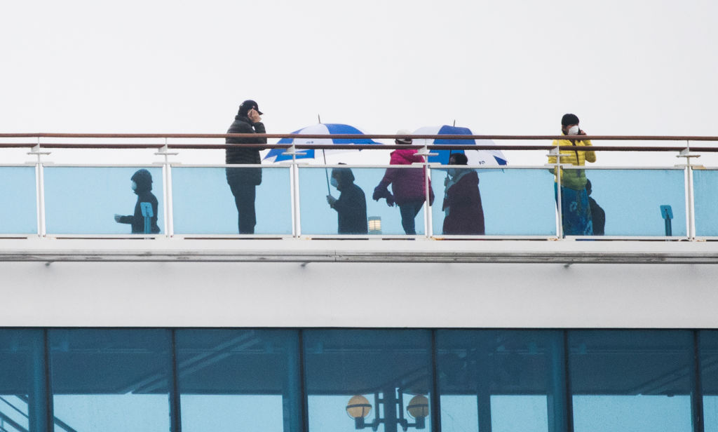 Passengers of the Diamond Princess cruise ship, who are quarantined due to fear of the new COVID-19 coronavirus, walk on the deck of the ferry docked at the Daikaku Pier Cruise Terminal in Yokohama port on February 16, 2020. - Americans began leaving a quarantined cruise ship off Japan on the night between February 16 and February 17, 2020 to board chartered flights home as the number of new coronavirus cases diagnosed on the vessel jumped to 355. (Photo by Behrouz MEHRI / AFP) (Photo by BEHROUZ MEHRI/AFP via Getty Images)