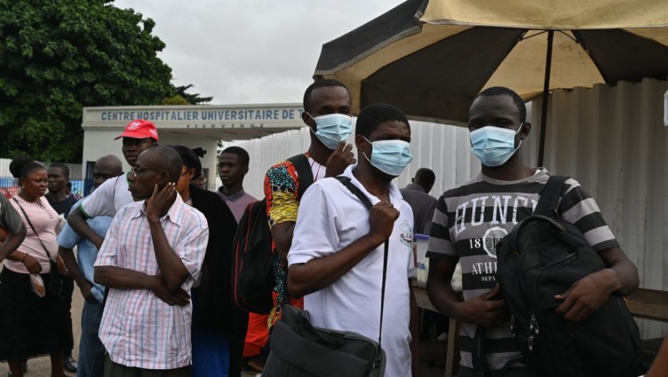TOPSHOT - People wear protective masks as they wait at a bus stop outside Treichville university hospital, on March 11, 2020, where the first Ivorian case of new coronavirus was confirmed. The Ivorian case is a 45-year-old man who had recently stayed in Italy, the government said on March 11, 2020. (Photo by ISSOUF SANOGO / AFP) (Photo by ISSOUF SANOGO/AFP via Getty Images)