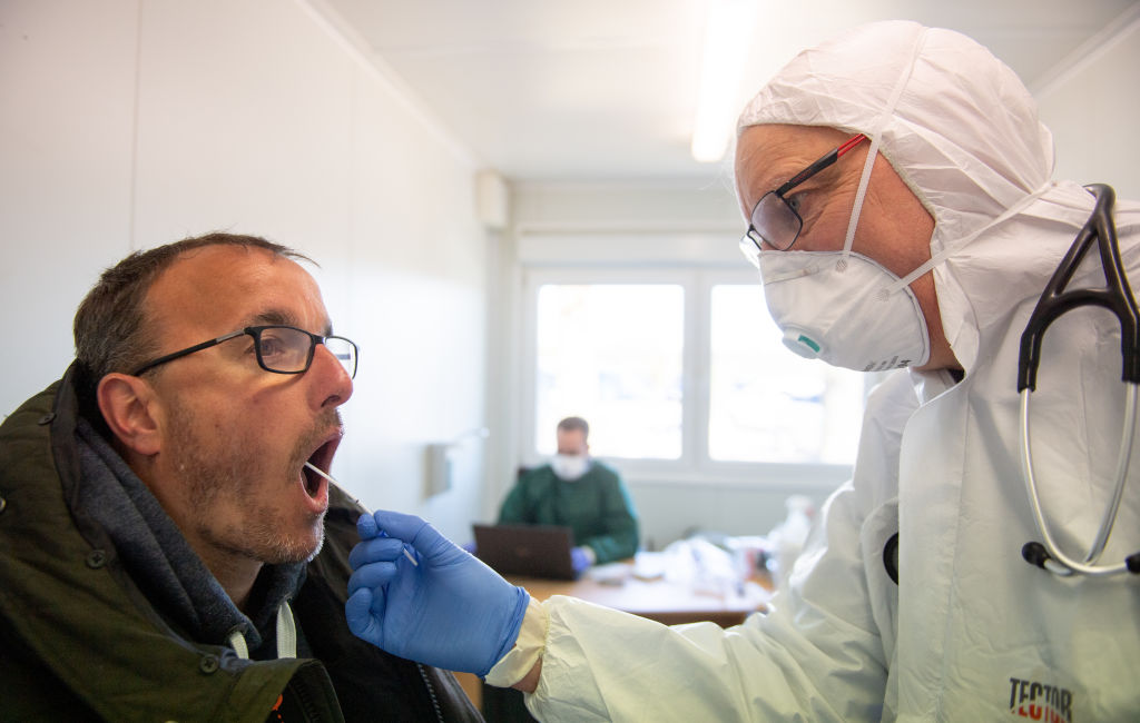 PAPENBURG, GERMANY - MARCH 23: Local doctor Volker Eissing peers into the throat of a patient while checking for flu and also to take a throat swab sample for coronavirus testing at Eissing's temporary office located in a container on March 23, 2020 in Papenburg, Germany. Eissing is using the container, located on a parking lot, in order to avoid possible coronavirus exposure for his colleagues at his regular practice. Around 50 people a day come to be tested for coronavirus and the disease the virus causes, COVID-19. Germany is struggling to reign in the spread of the coronavirus, which so far has infected at least 24,000 people nationwide. (Photo by David Hecker/Getty Images)