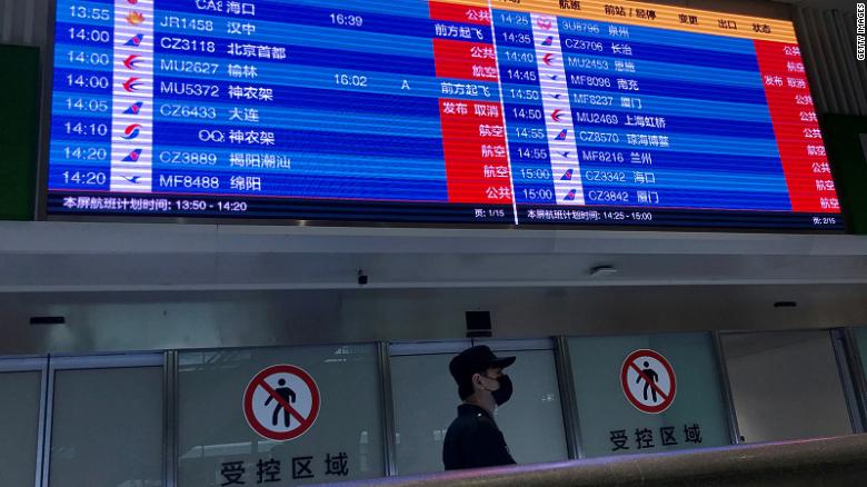 A man wearing a facemask stands under a screen showing mostly cancelled flights at Tianhe airport in Wuhan in China's central Hubei province on January 23, 2020. - China banned trains and planes from leaving a major city at the centre of a virus outbreak on January 23, seeking to seal off its 11 million people to contain the contagious disease that has claimed 17 lives, infected hundreds and spread to other countries. (Photo by Leo RAMIREZ / AFP) (Photo by LEO RAMIREZ/AFP via Getty Images)